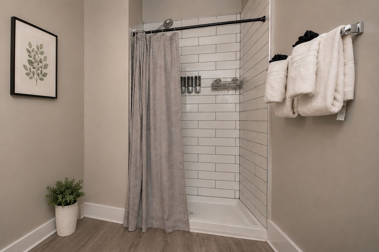 Eine Dusche mit grauer Duschvorhang, einer weiß gefliesten Wand, einer Topfpflanze und einem Handtuchhalter mit Handtüchern.