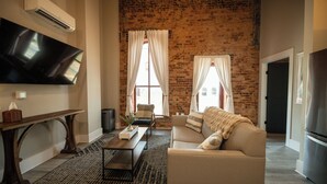 A living room with a brick wall, a flat-screen TV, a sofa, a coffee table, and a fireplace. - Three Trails Downtown Elkin (Elkin)