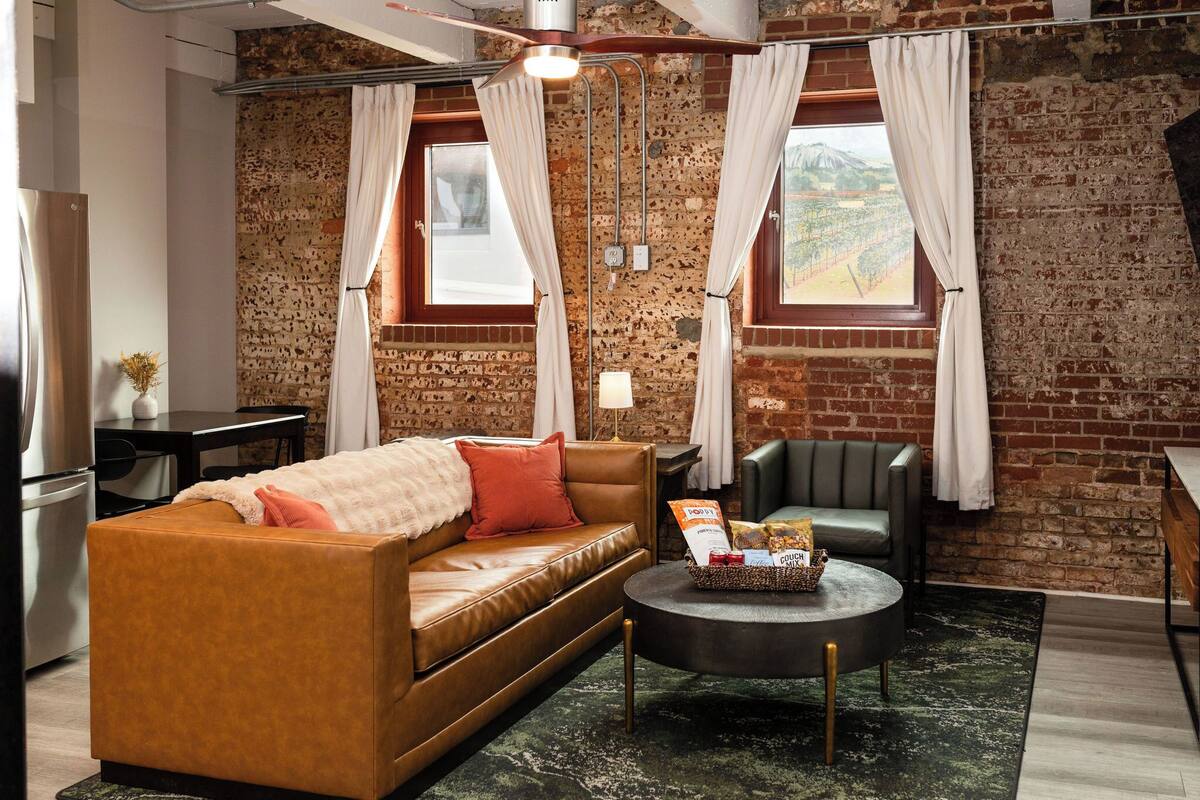 Una sala de estar acogedora con un sofá de cuero, una mesa de centro redonda y una pared de ladrillo.