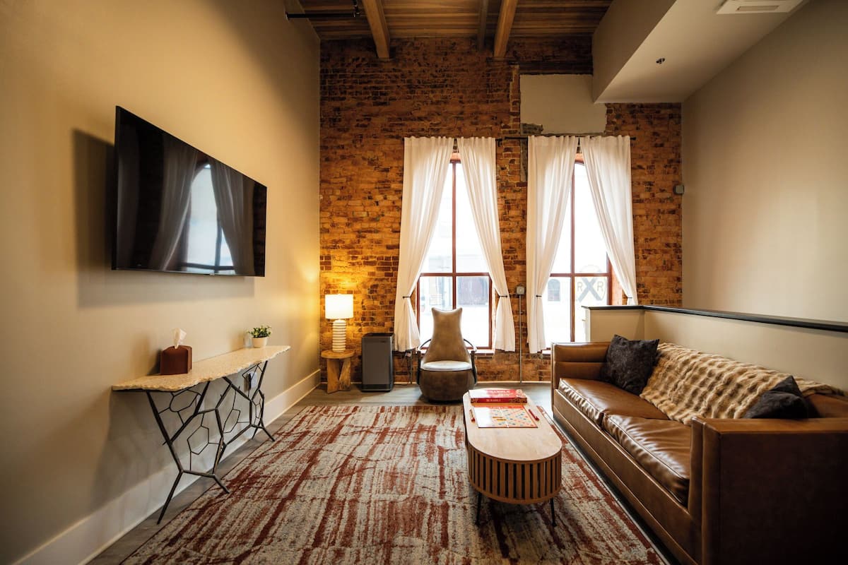 Una sala de estar con pared de ladrillo, televisión de pantalla plana, sofá, mesa de centro y lámpara.