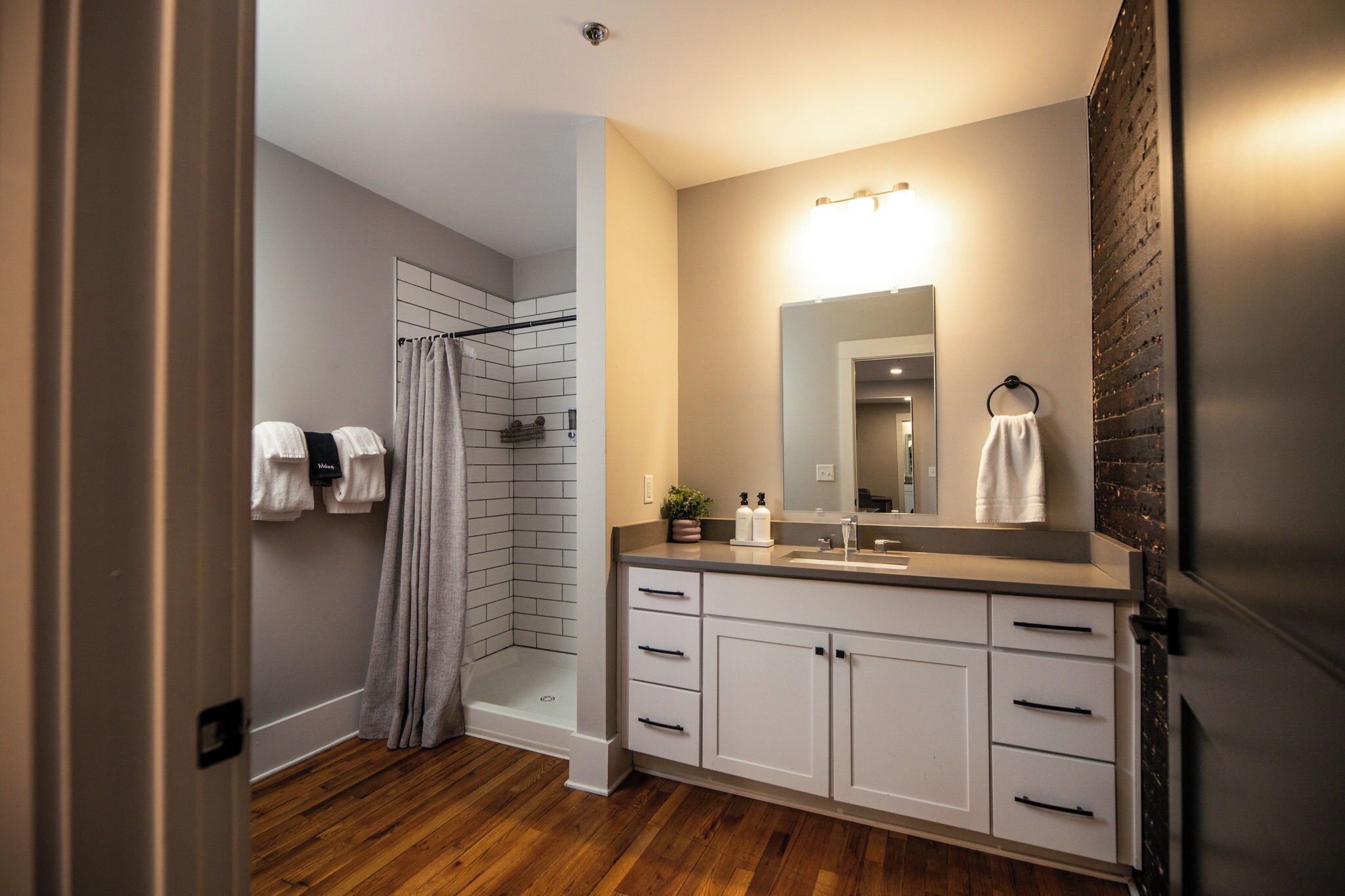 Une salle de bain moderne avec une douche, un lavabo avec un miroir et un plancher en bois.