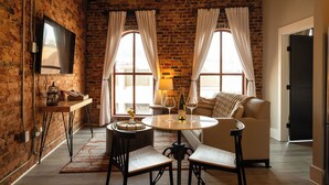 A cozy room with a brick wall, a round table with chairs, a sofa, and a TV mounted on the wall. - Three Trails Downtown Elkin (Elkin)