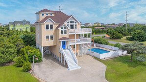 A two-story house with a balcony, a swimming pool, and a basketball hoop. - Soundside Dog Friendly Home w/ Pool, Hot Tub, Game Room, Tiki Bar, Public Dock (Rodanthe)