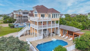 A multi-story house with a pool, outdoor seating, and a covered barbecue area. - Soundside Dog Friendly Home w/ Pool, Hot Tub, Game Room, Tiki Bar, Public Dock (Rodanthe)
