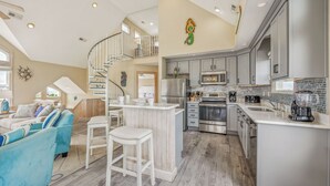 A spacious kitchen with modern appliances, a central island, and a dining area with a blue sofa. - Soundside Dog Friendly Home w/ Pool, Hot Tub, Game Room, Tiki Bar, Public Dock (Rodanthe)