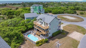 A large, multi-story house with a swimming pool, surrounded by dense greenery and a view of the ocean. - Soundside Dog Friendly Home w/ Private Pool, HotTub, Game Room, Community Tennis (Avon)