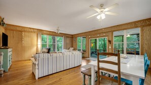 Un interior de madera con sofá, mesa de comedor, sillas, ventiladores de techo y ventanas grandes.