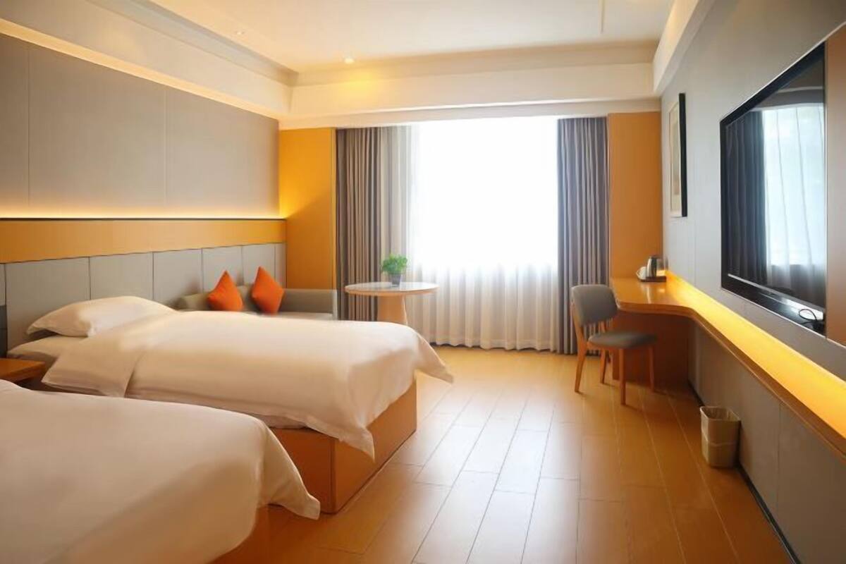 A hotel room with two beds, a desk, a chair, a TV, and a window with curtains.