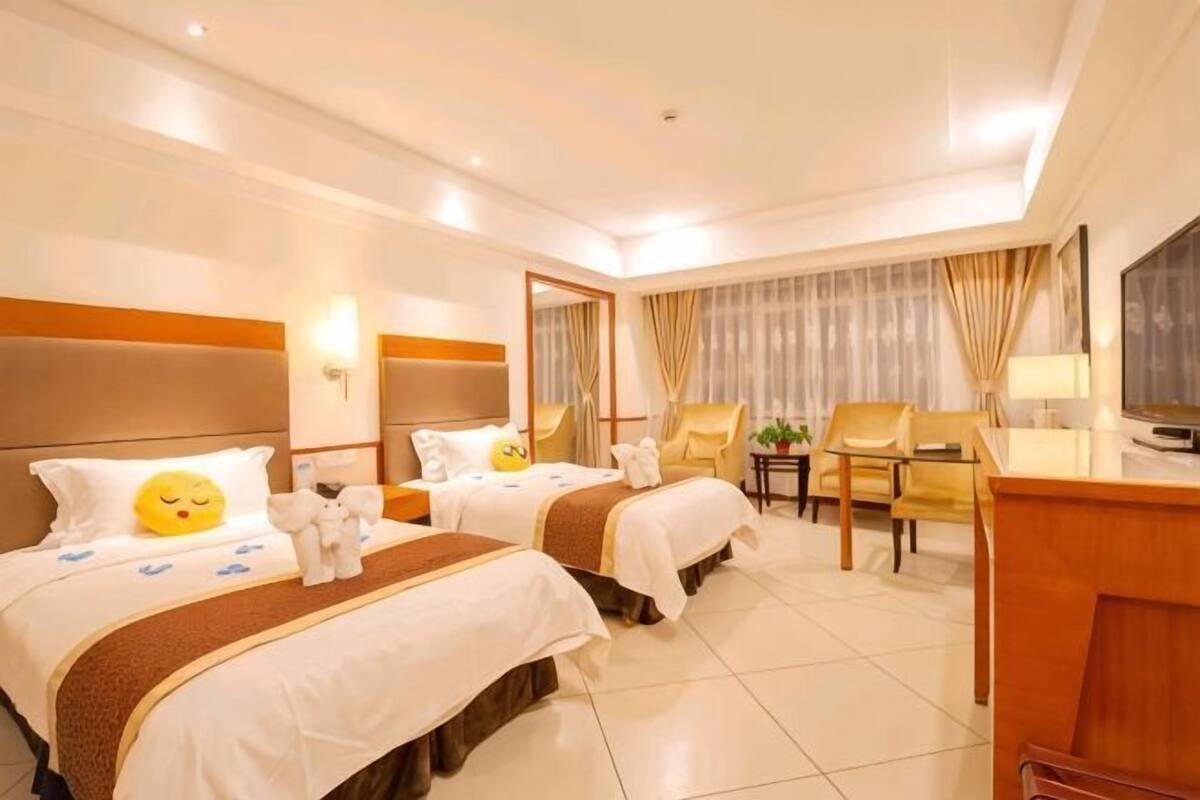 A hotel room with two beds, a desk, a chair, a TV, and a window with curtains.