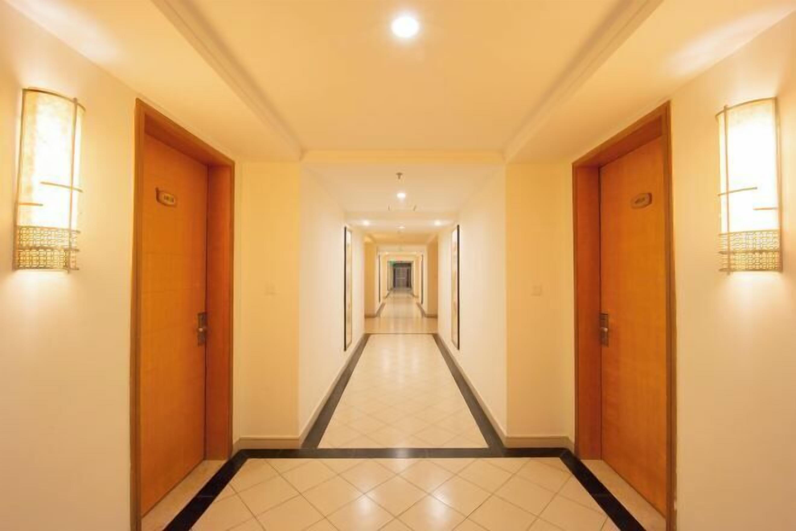 A hotel hallway with wooden doors, tiled flooring, and wall-mounted light fixtures.
