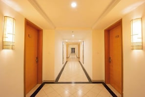 A hotel hallway with wooden doors, tiled flooring, and wall-mounted light fixtures. - Beichen Hotel (Haikou)