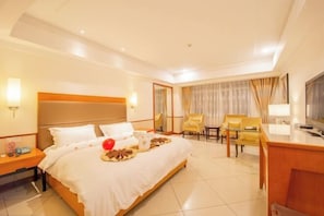 A hotel room with a bed, bedside tables, a desk, chairs, and a television.