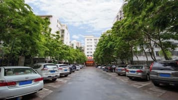Una calle bordeada por coches aparcados y árboles, que conduce a un edificio con un letrero rojo.