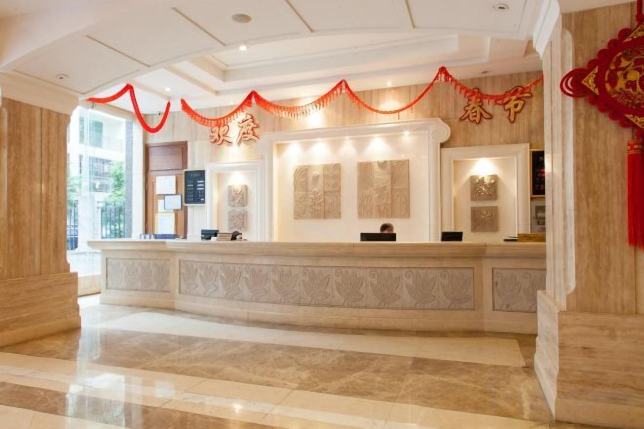 Zona de recepción de un hotel con mostrador de mármol, obras de arte enmarcadas y detalles decorativos en rojo.