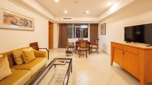 A living room with a sofa, coffee table, TV, dining table, chairs, and artwork on the walls. - Beichen Hotel (Haikou)