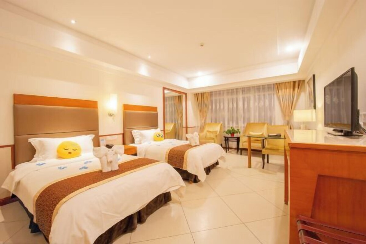 A hotel room with two beds, a desk, a chair, and a television.