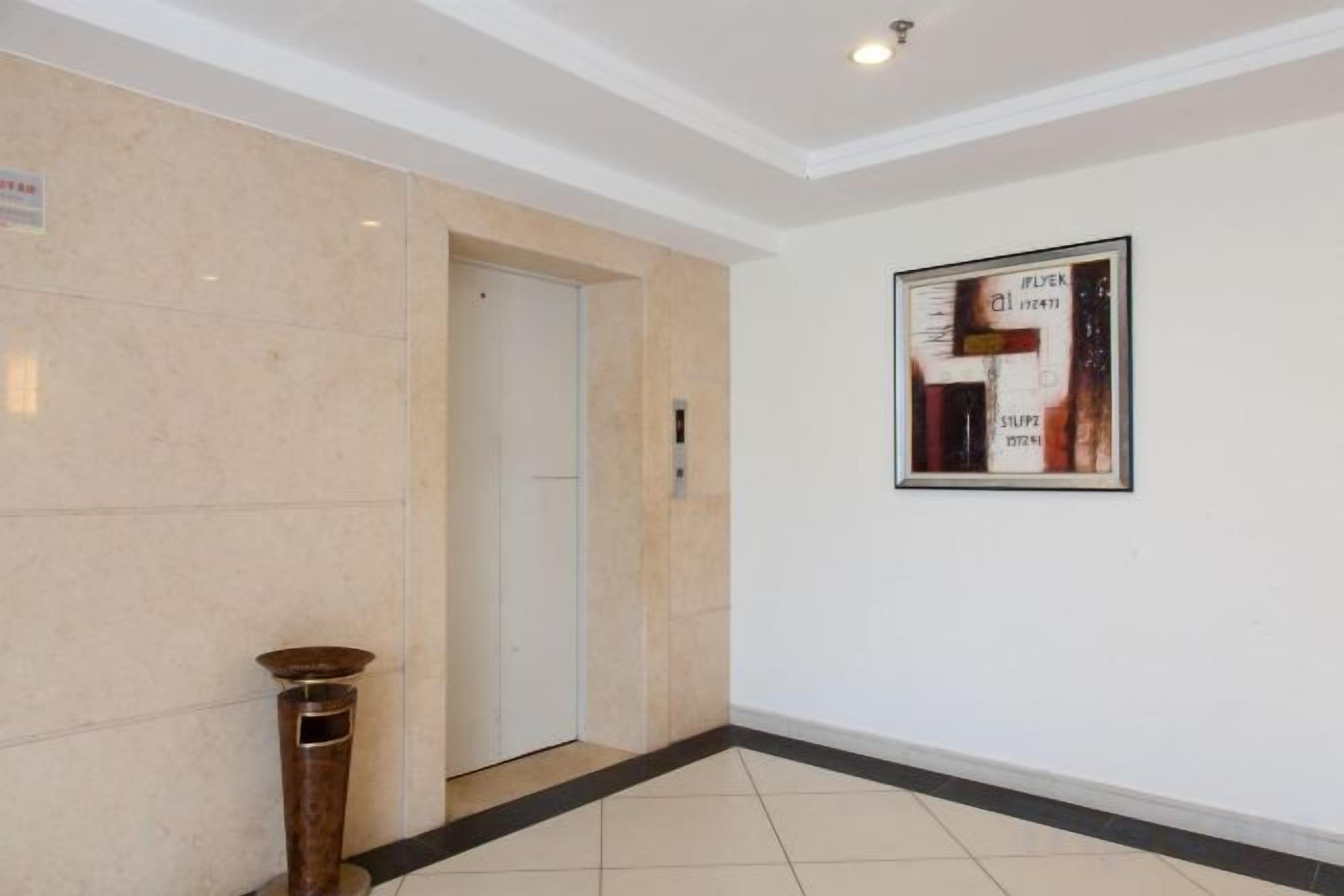Un pasillo con una puerta, un cuadro enmarcado en la pared y piso de baldosas.