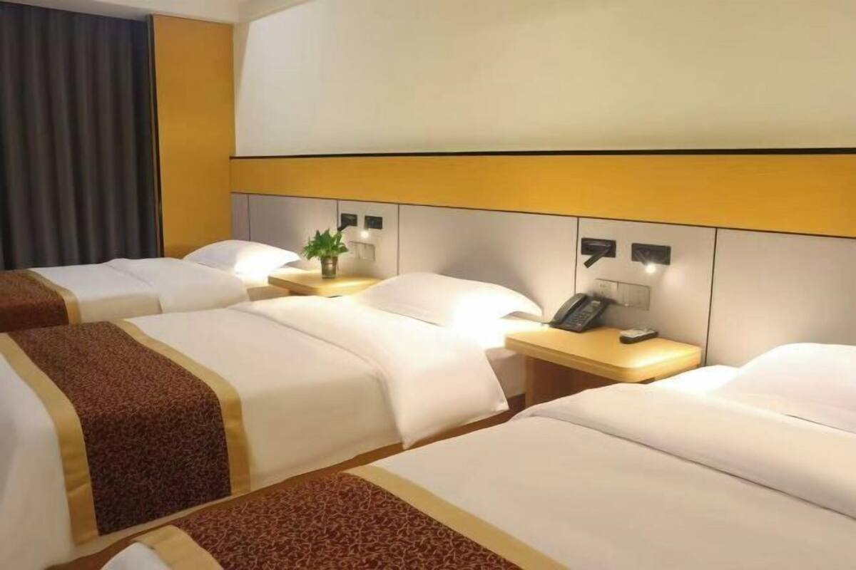 A hotel room with three beds, a bedside table with a lamp, and a phone.