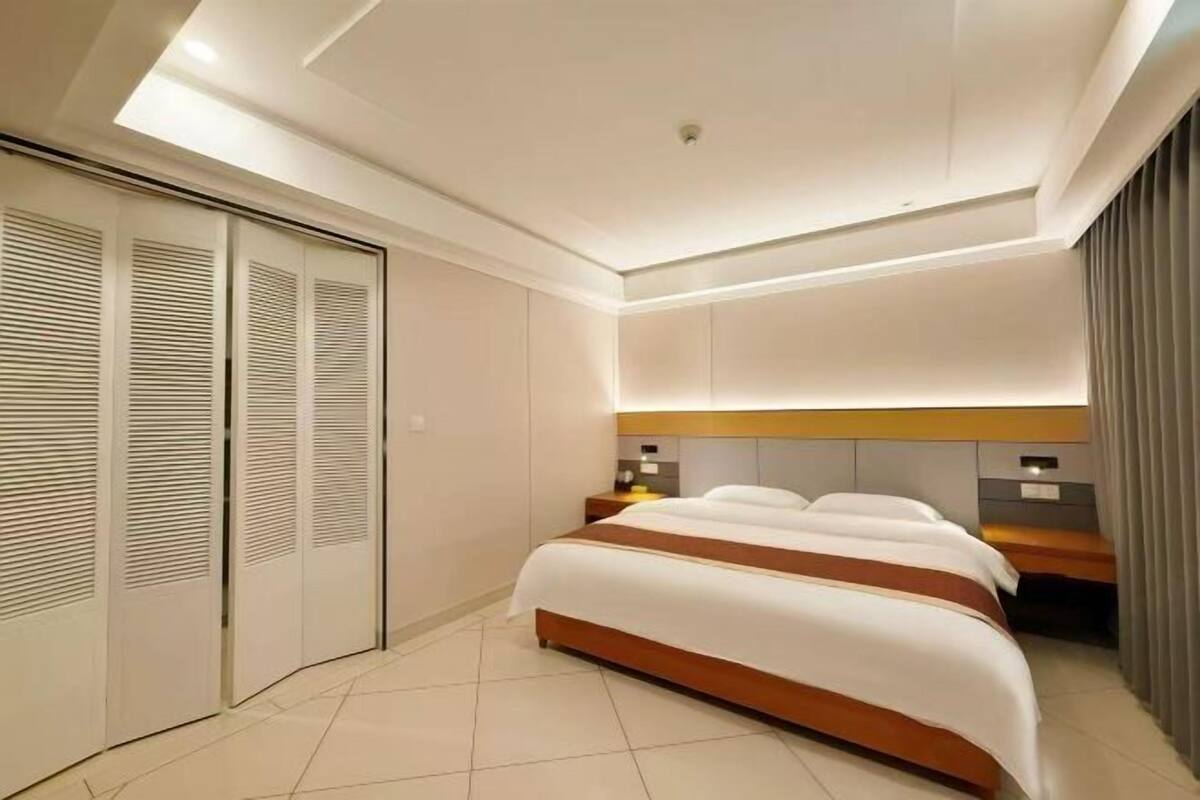 A modern hotel room with a large bed, a bedside table, a wardrobe, and a ceiling light.