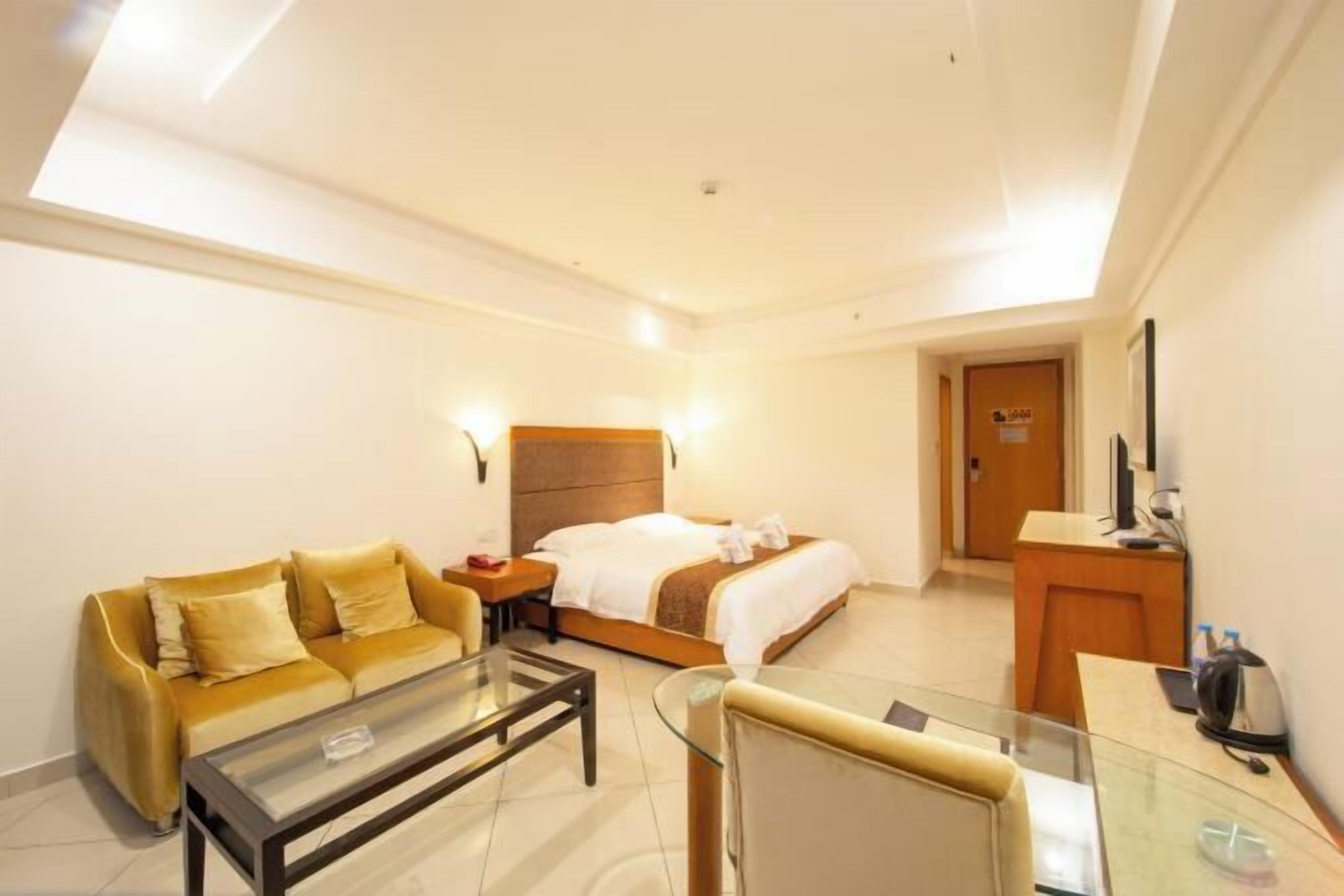 A hotel room with a bed, a sofa, a glass coffee table, a desk, and a TV.