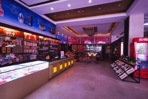 A brightly lit retail store with shelves stocked with various products, a display counter, and promotional posters on the walls. - Beichen Hotel (Haikou)