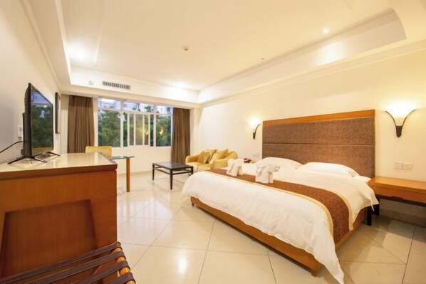 A hotel room with a large bed, a desk, a sofa, and a TV.