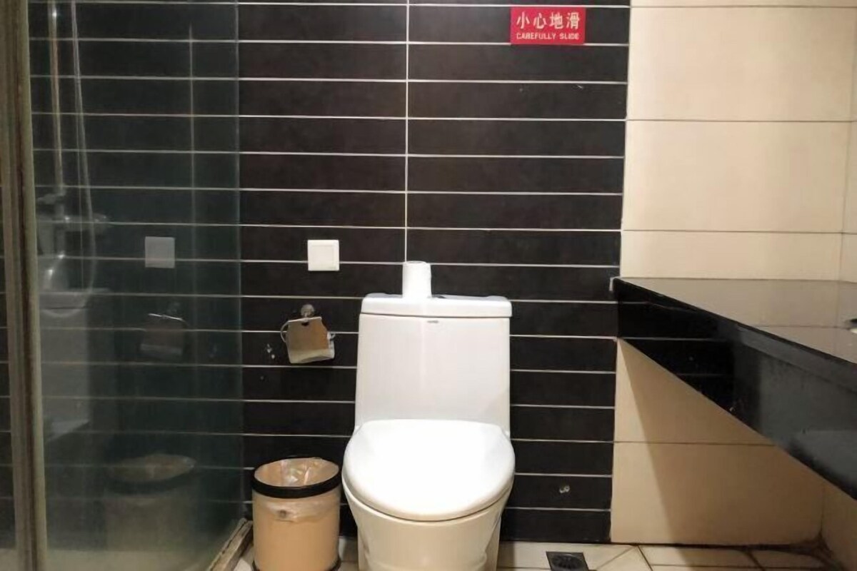 A bathroom with a toilet, a trash bin, and a hand dryer.