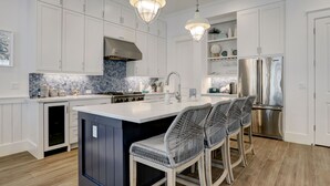 Una cocina moderna con armarios blancos, una isla central con taburetes de bar, electrodomésticos de acero inoxidable y un backsplash de azulejos azules.