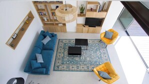 Een moderne woonkamer met een blauwe bank, gele fauteuils, een salontafel, een televisie en een boekenkast.