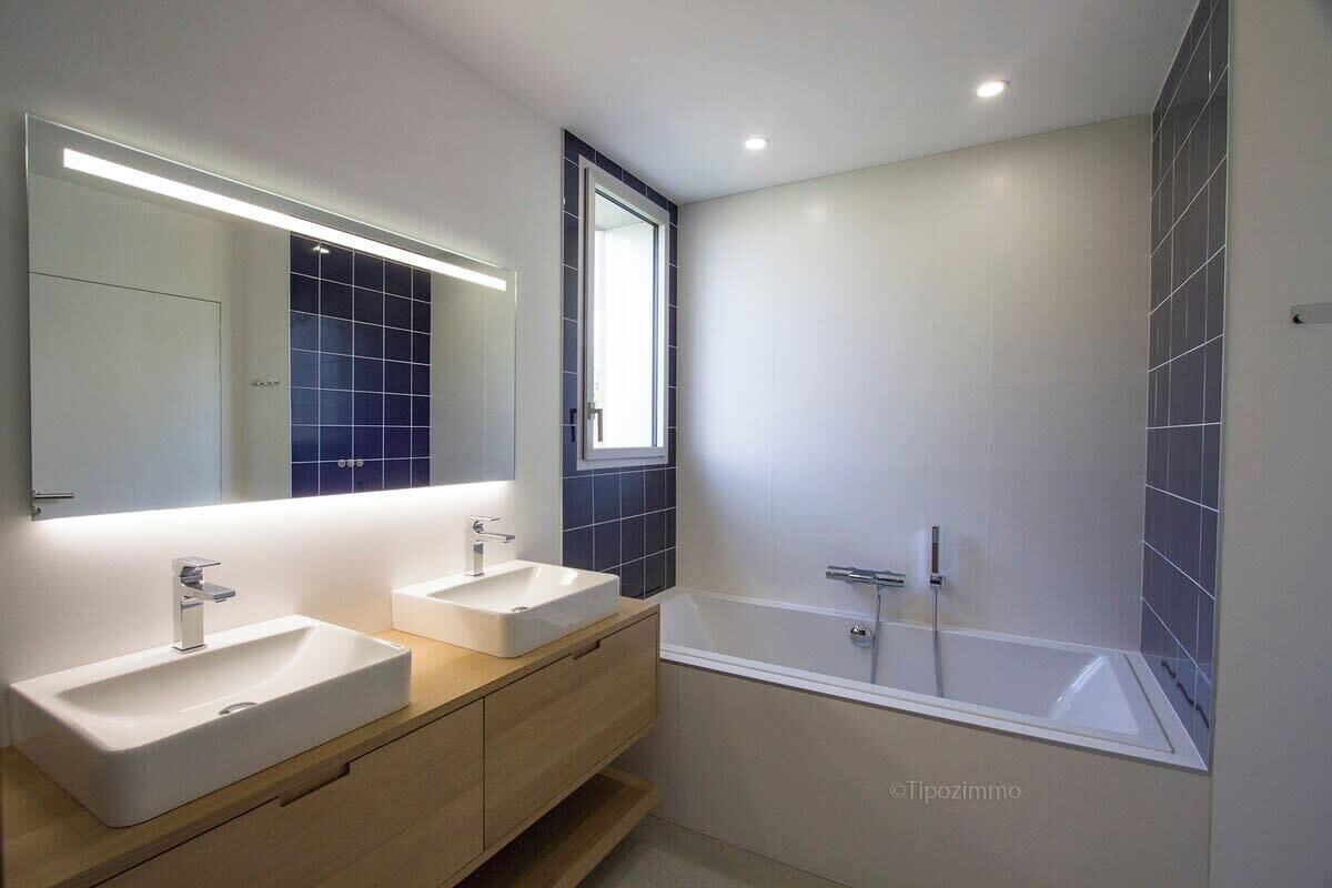 Une salle de bain moderne avec deux lavabos, un grand miroir et une baignoire.