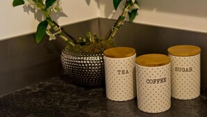A kitchen counter with a decorative white flower arrangement, a textured pot, and three labeled containers for tea, coffee, and sugar.