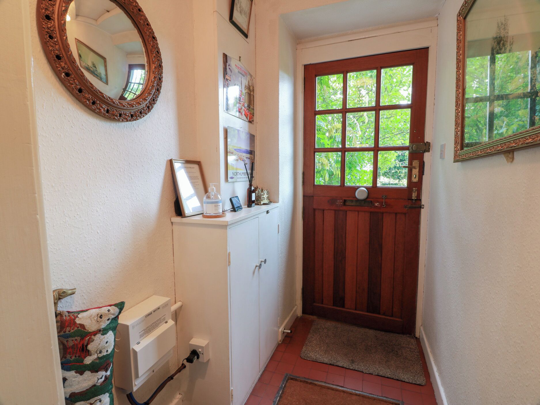 A narrow hallway with a wooden door, a white cabinet, a mirror, and a framed picture on the wall.