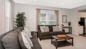 A living room with a dark brown sofa, a coffee table, and a large window with curtains.