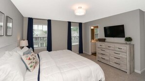 A bedroom with a bed, a dresser, a TV, and a window with curtains.
