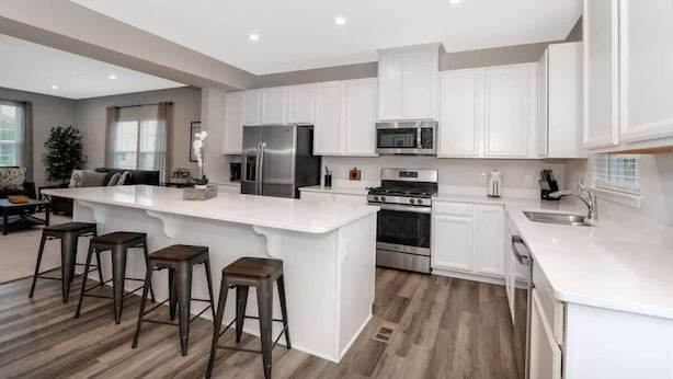 A modern kitchen with white cabinetry, stainless steel appliances, and a central island with bar stools.