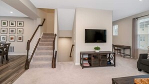 A spacious living room with a staircase, a flat-screen TV mounted on the wall, a dining area, and a sofa.