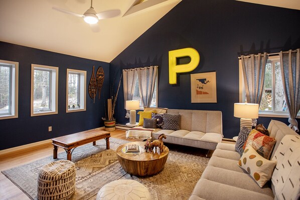 Un salon avec un mur bleu foncé, une grande décoration en forme de « P », un canapé, une table basse et un banc en bois.