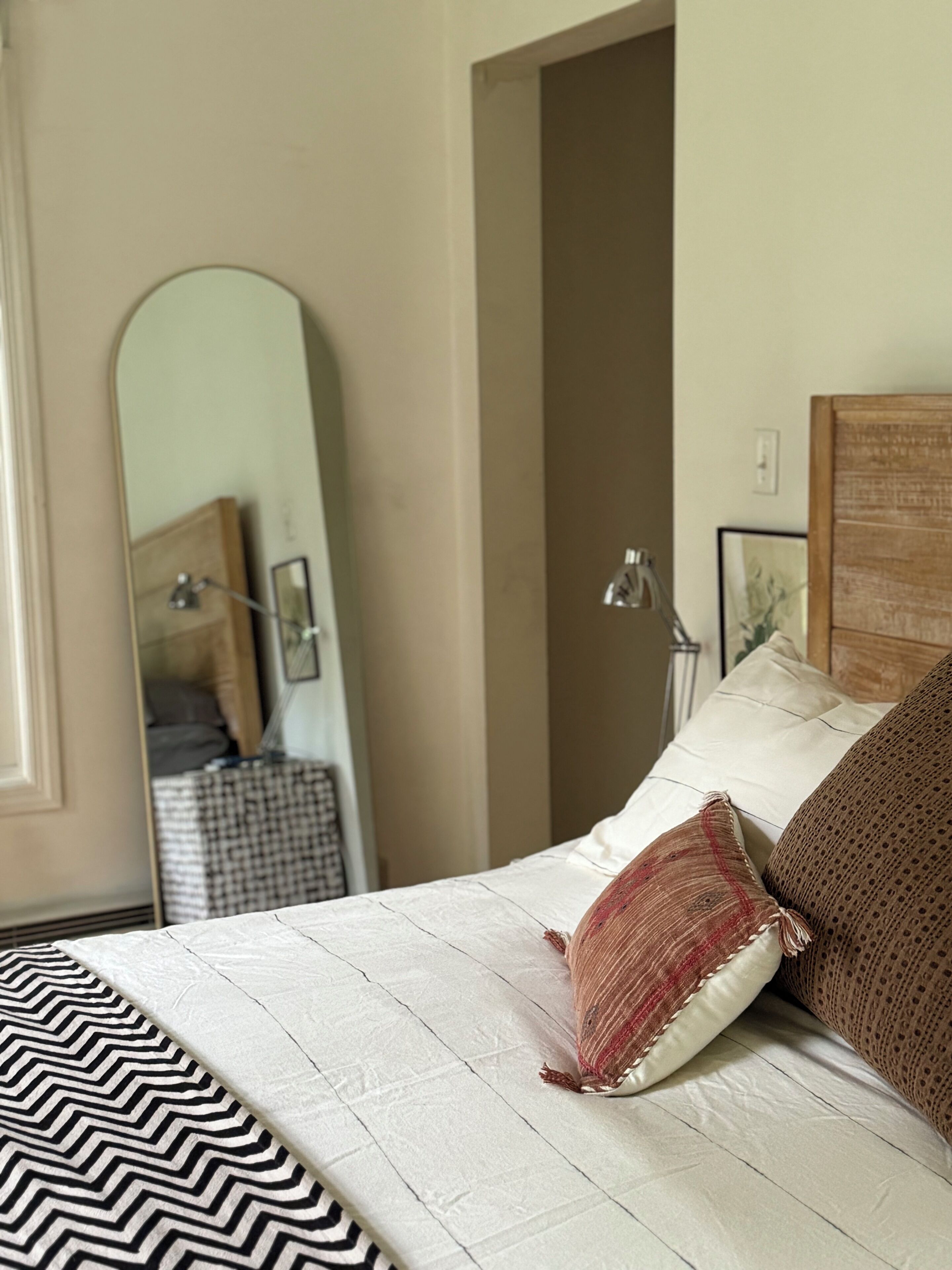 Een slaapkamer met een bed, een spiegel, een deur en een nachtkastje.