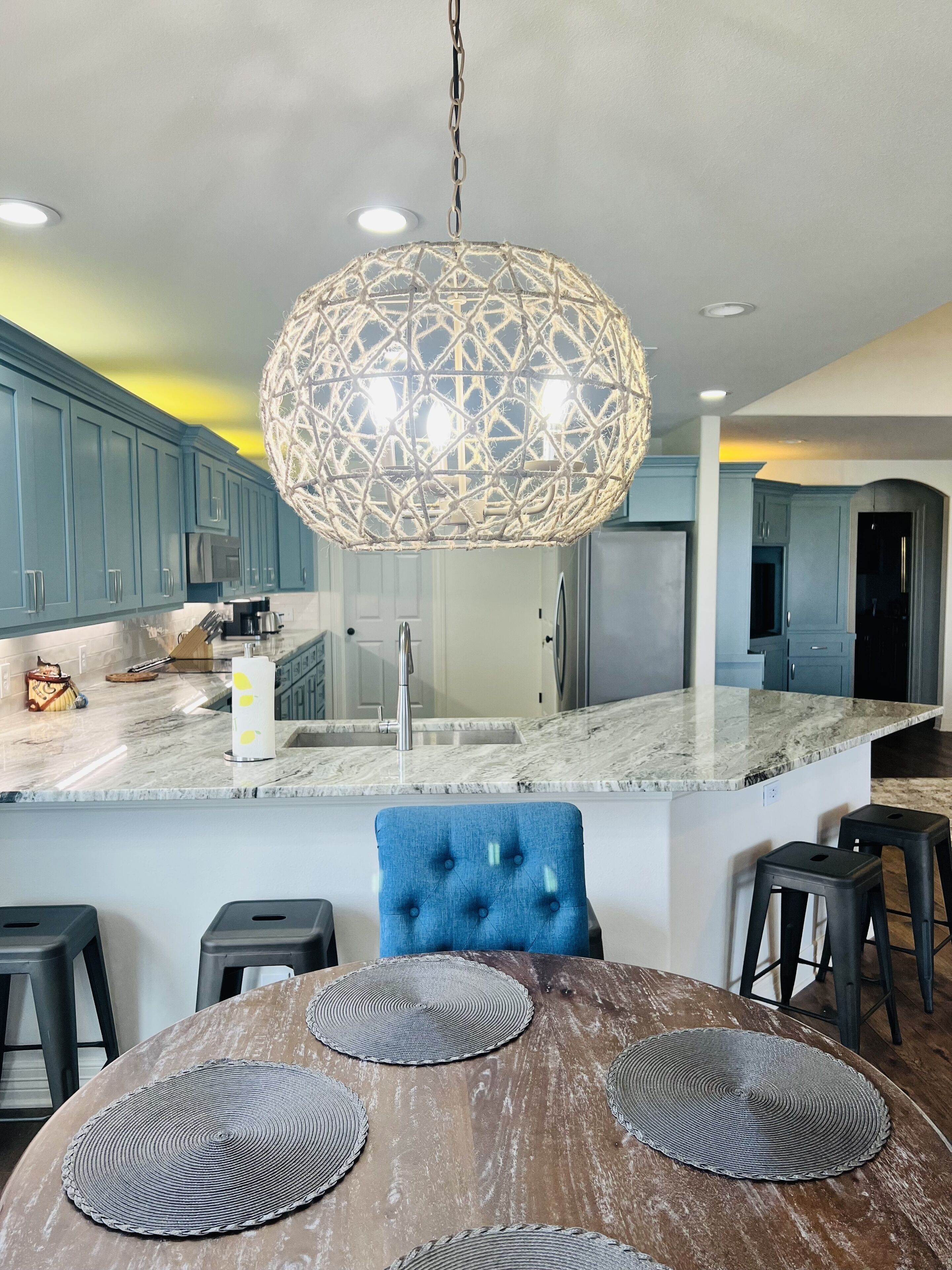Une cuisine moderne avec des meubles bleus, un plan de travail en marbre et un luminaire suspendu au design géométrique original.
