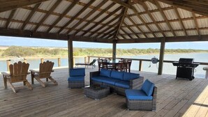 A covered outdoor deck with wicker furniture, a grill, and a view of a body of water. - River Rendezvous! Newly renovated with newly  constructed boathouse (Matagorda)