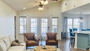 A spacious living room with a large round coffee table, two leather armchairs, a sofa, and a ceiling fan. - River Rendezvous! Newly renovated with newly  constructed boathouse (Matagorda)