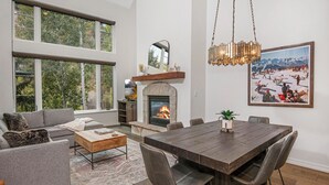 A spacious living room with a fireplace, large windows, and a dining area with a wooden table and chairs. - Absolutely Darling Condo w/ Very Short Walk to Arrowhead Lift, Pool, Hot Tub!! (Edwards)