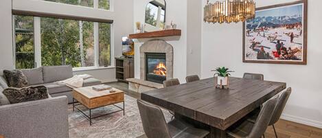 A spacious living room with a fireplace, large windows, and a dining area with a wooden table and chairs.