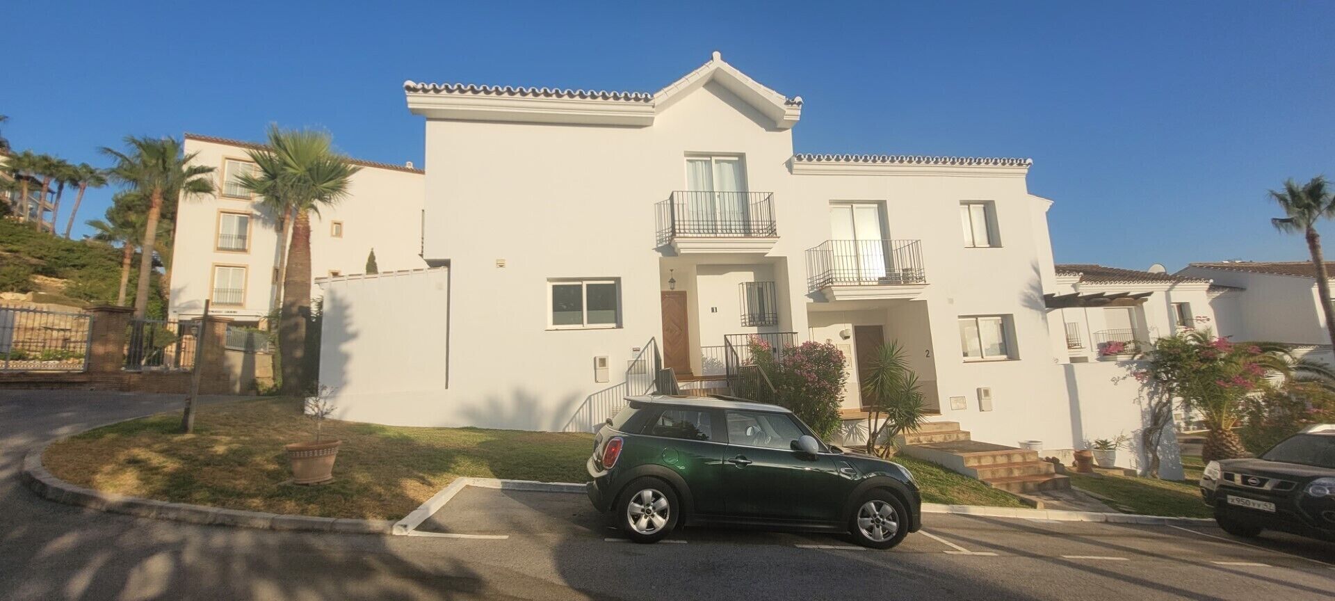 Um edifício residencial de dois andares com varanda, entrada para carros e um carro estacionado.