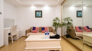 Ein Zimmer mit einem beigefarbenen Sofa, das mit Kissen mit amerikanischer Flagge geschmückt ist, einem weißen Couchtisch, einem Schreibtisch mit Stuhl und einem großen Spiegel an der Wand.