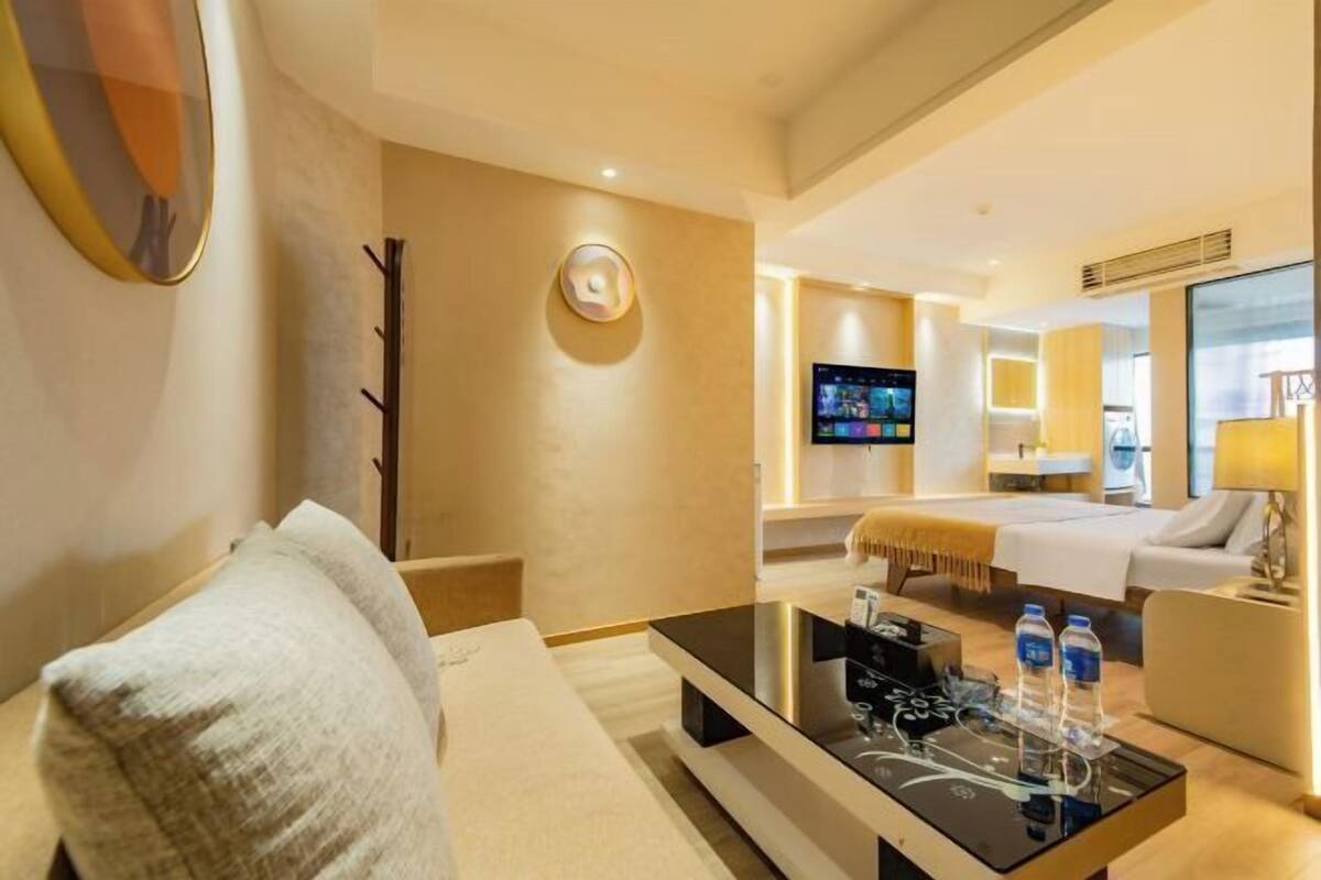 Une chambre d’hôtel avec un lit, une télévision, une table basse avec des bouteilles d’eau et un canapé.