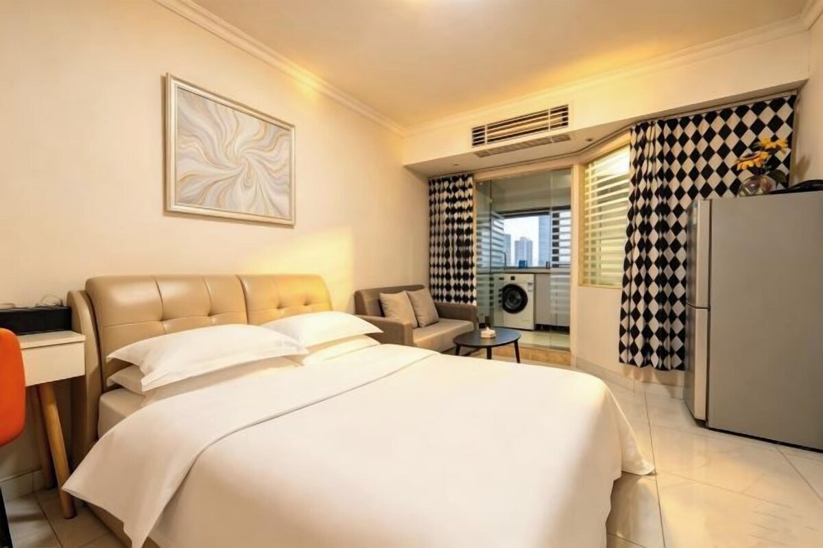 Una habitación de hotel con cama, escritorio, silla, mesita y refrigerador.