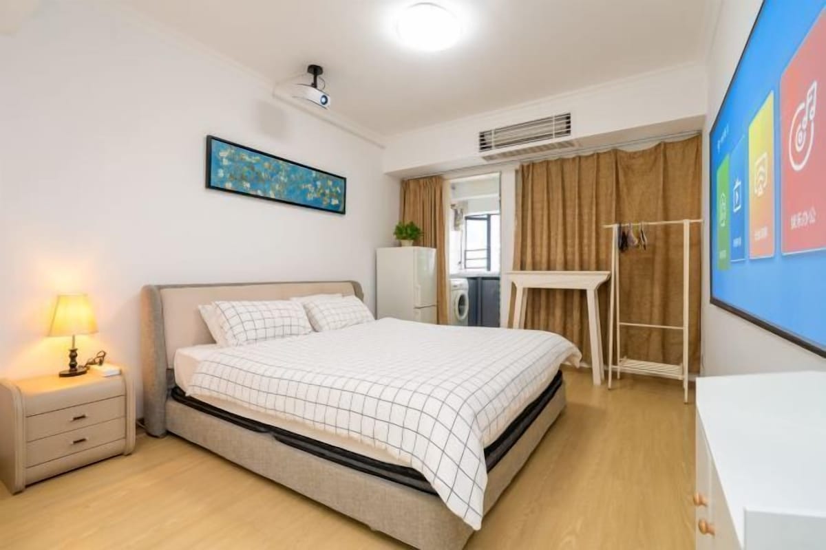 A bedroom with a bed, bedside table, and a wall-mounted projector.