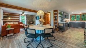A modern kitchen with a stone fireplace, wooden beams, and a dining area with a round table and chairs.
