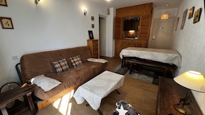 A cozy living room with a brown sofa, a wooden table, a bench, and a small kitchen area with wooden cabinets. - VIKING 23 - Village center apartment - Parking (La Clusaz)